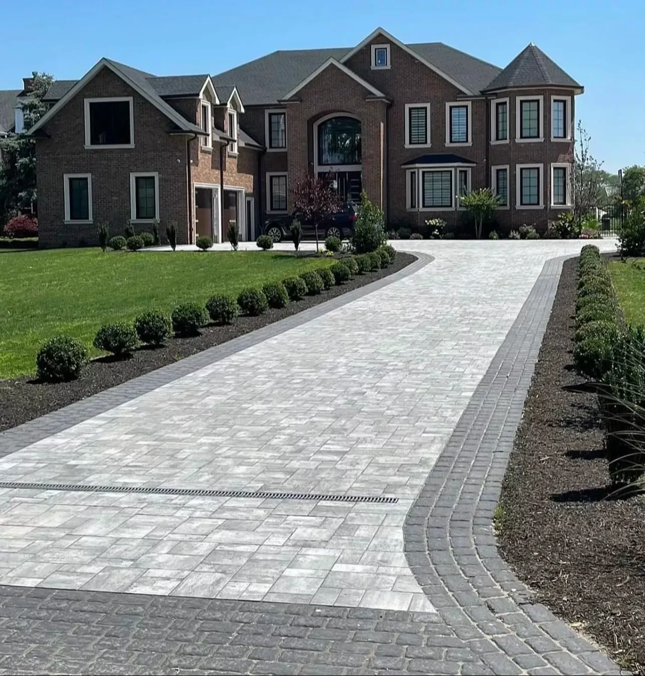 Large paver driveway leading to a brick home